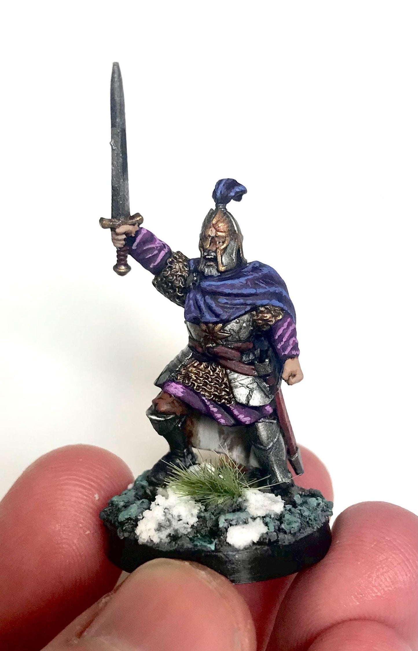 Miniature dark fantasy figurine of a warrior holding a sword, held between fingers on a white background